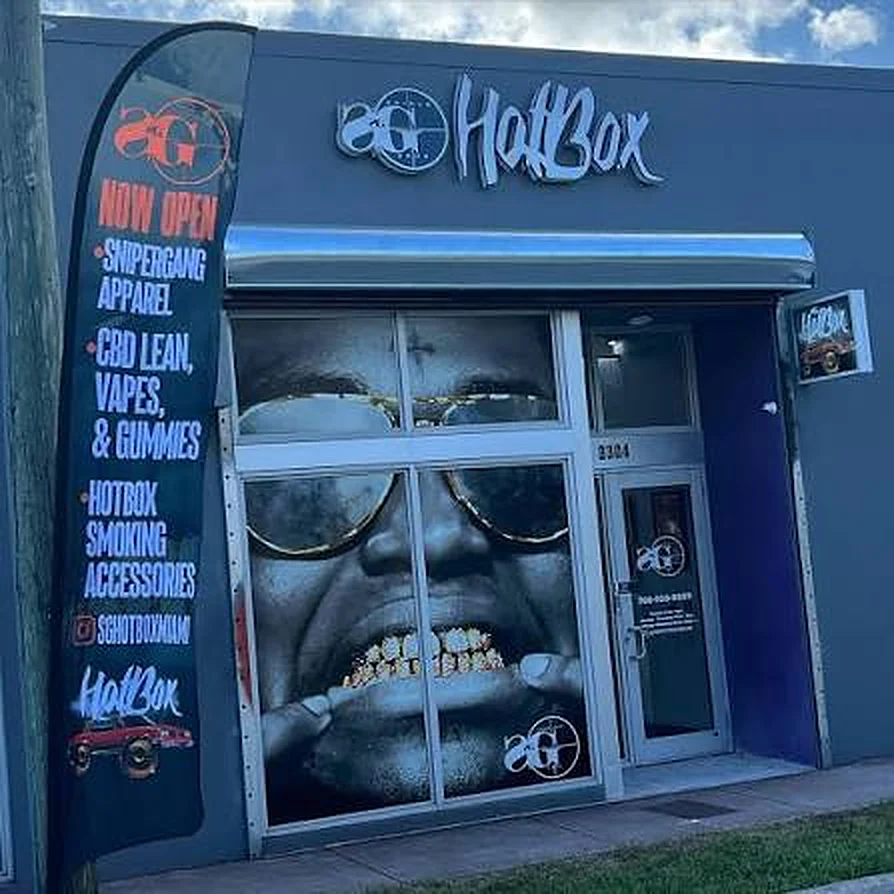 The SG HotBox storefront, windows wrapped with a gold grill smile, 'Now open' banner out front